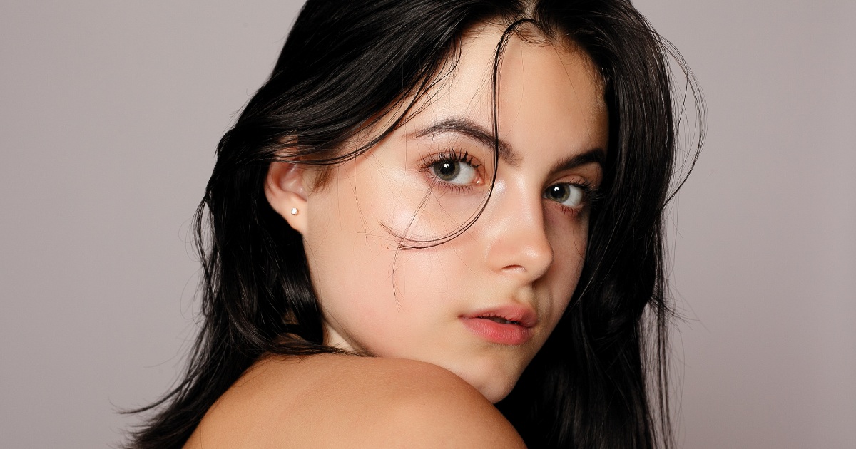 A woman with a a close-up portrait of a young woman with long dark hair and clear, glowing skin.
